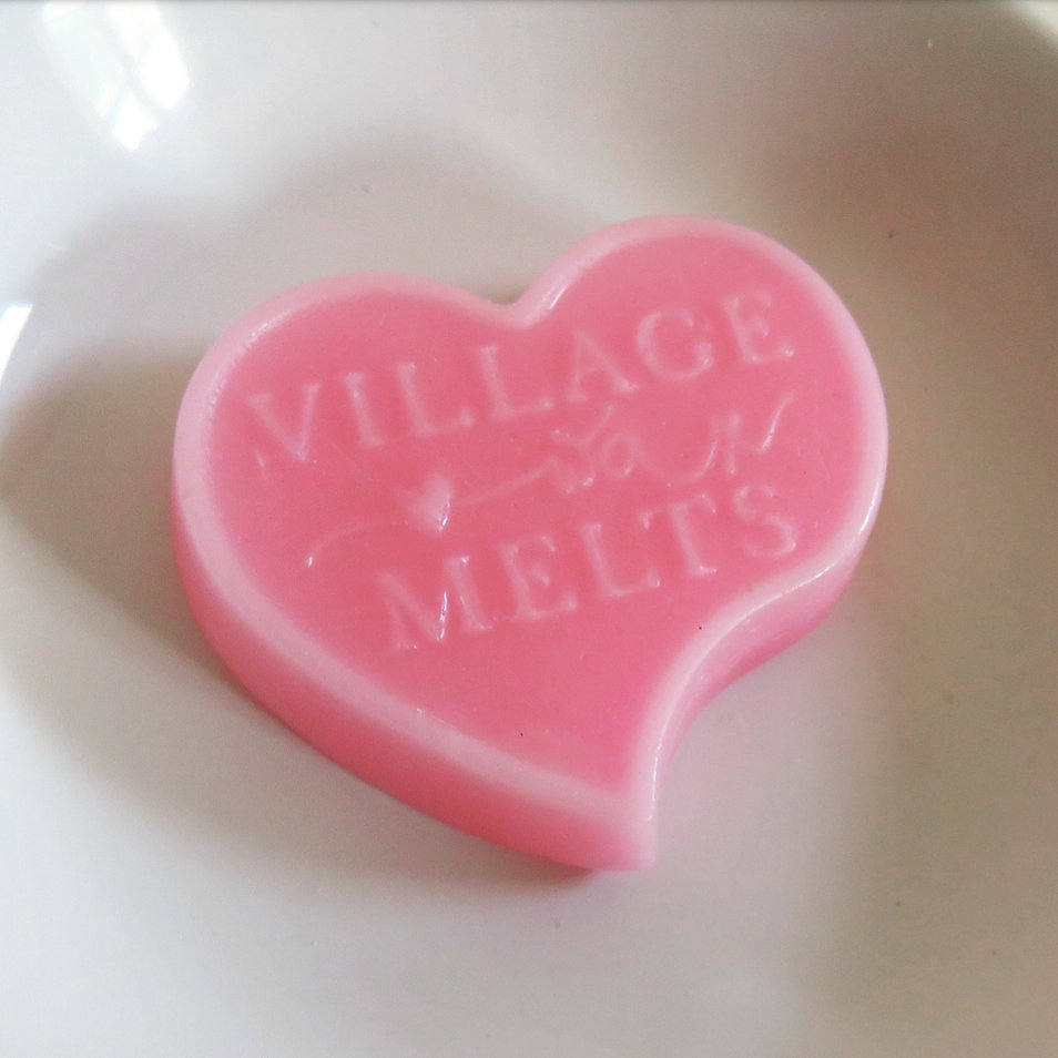 A pink Village Wax Melts heart shaped melt embossed with the brand name